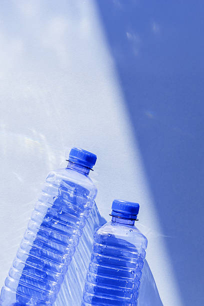 istock Clear plastic water bottles for clean water on white blue background closeup, minimal aesthetic lifestyle photo, top view, flat lay, Naural light, sunlight shadows, caustic light effect, star filter 2241325889