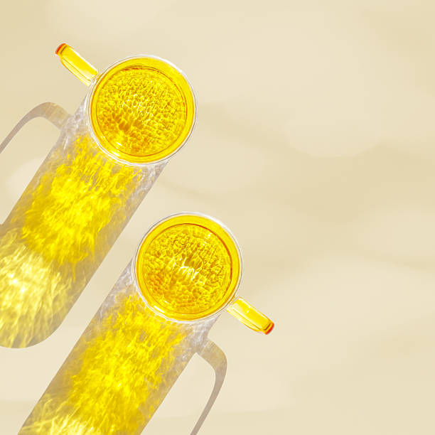 istock Top view of two yellow colored glass mugs creating vivid light reflections and caustics on beige background. Transparent cup at sunlight with sun glare, summer drink photo, golden tones, copyspace 2241325924