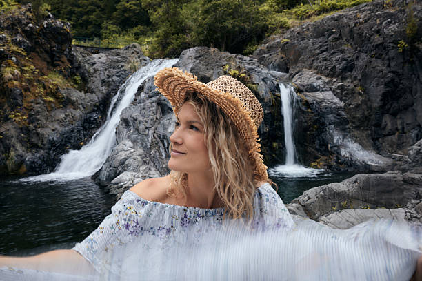 Smiling woman having fun while day dreaming by the waterfall in nature. Blurred motion.