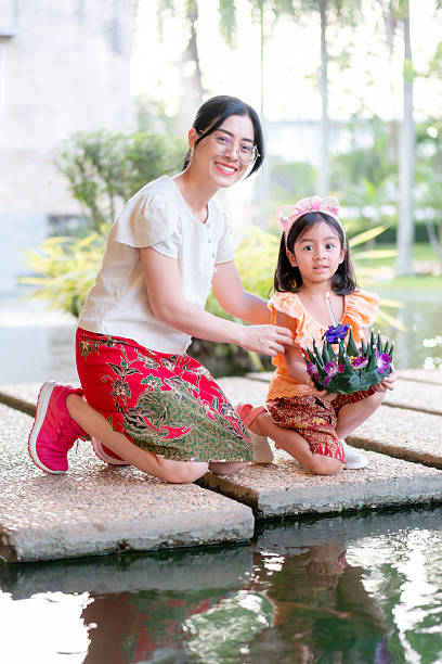 Thai Mother and Daughter Preparing to Float a Krathong in a Pond, Celebrating the Beautiful Loy Krathong Festival.