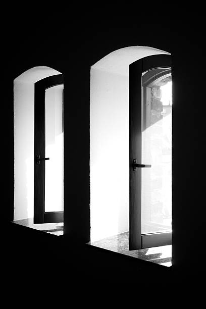 istock Black and white photo of arched windows with open frames in a dark interior. Minimalist architectural composition with strong contrast of light and shadow. 2241332112