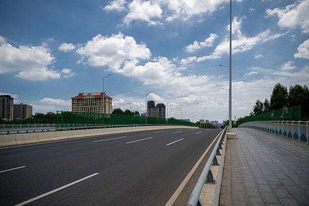 A Wide Road Alongside a City Highway Under a Blue Sky with White Clouds