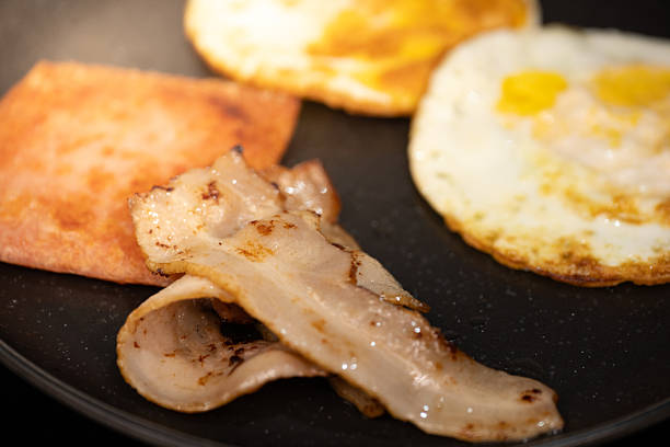 istock Crispy Bacon Slices Served with Sunny-Side-Up Eggs and Toast on a Black Plate 2241334566