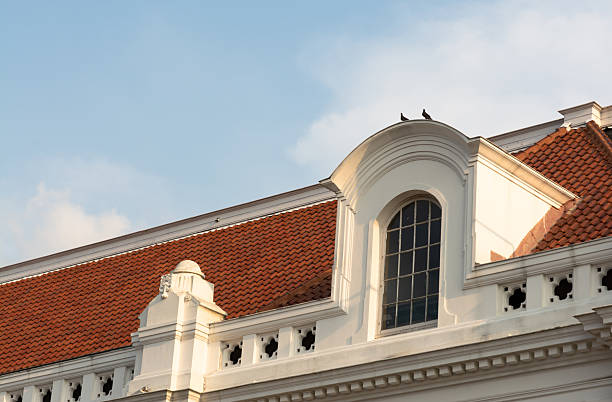 image of a Dutch colonial building showcasing detailed rooftop tiles and classic attic windows illuminated by warm afternoon sunlight. The architectural design reflects European colonial influence with its distinctive structure and symmetry. Captured under a clear blue sky, this image highlights heritage architecture and timeless charm, perfect for historical, cultural, or architectural editorial use.
