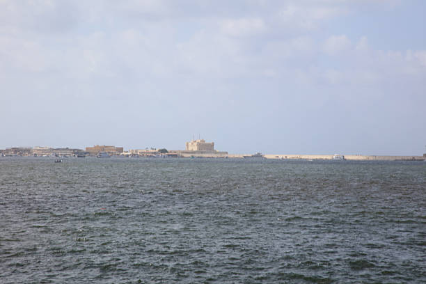 An overhead shot shows a long pier or breakwater cutting through vivid turquoise water, with waves breaking along the edges. The image conveys scale, calm yet powerful ocean energy, and man-made structure meeting the sea.