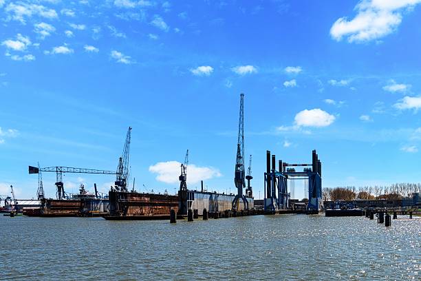A striking view of a shipyard featuring towering cranes, strong structures, and glistening water, all under a bright blue sky with scattered clouds. Perfect for industrial project inspiration.