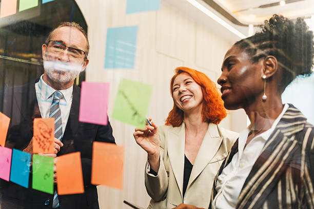 istock Diverse coworkers brainstorming with colorful sticky notes on a glass wall in a modern office, smiling and collaborating during a creative planning meeting. 2241343556