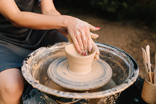 istock Potter shaping clay bowl on a wheel. Clay spins gently under hands as potter forms bowl. Clay molding on the wheel highlights pottery artistry and skill. 2241343950