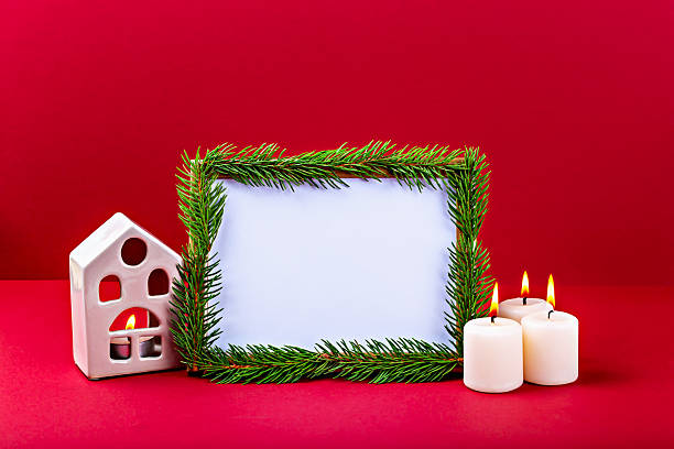 istock Festive holiday frame decorated with pine branches, candles and decorative house on red background 2241344830
