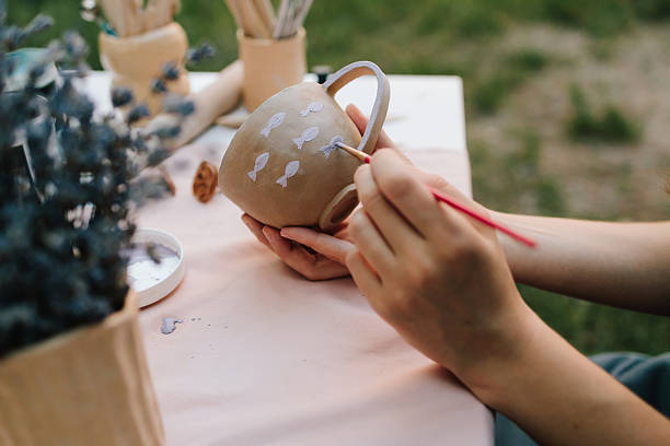 istock Ceramic painting of mug with fish pattern using brush strokes. Artist paints delicate purple fish on a handmade clay mug. Painting ceramic mug with purple fish using brush and paint. 2241345241