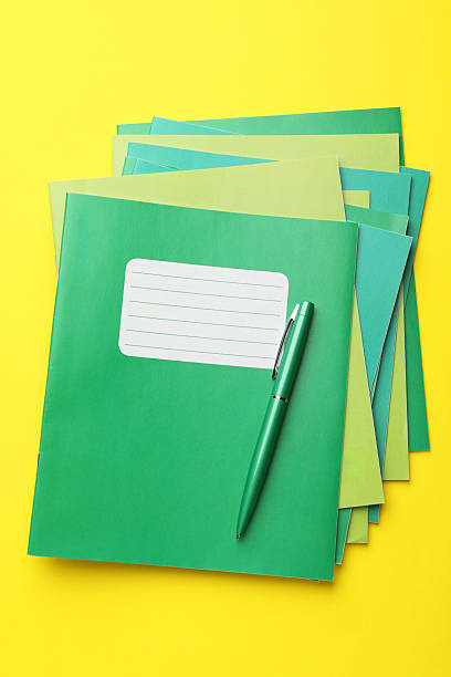istock Stack of copybooks and pen on yellow background, top view 2241350720