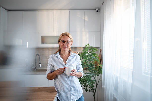 istock Mature woman smiling in modern kitchen holding coffee mug 2241352320