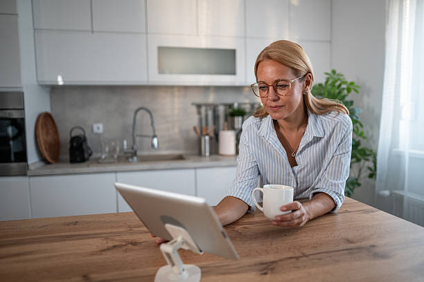 istock Mature woman drinking coffee while working on tablet at home 2241352335