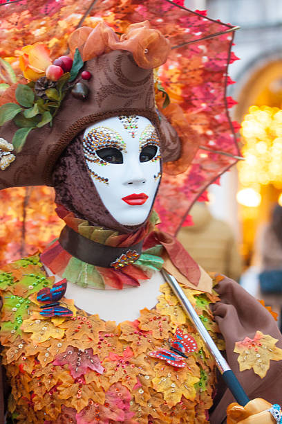 Venice, Italy - February 11, 2024: Close-up of a person wearing an elaborate venetian mask and floral headpiece, holding a black and gold fan during Carnival celebrations in Venice, Italy, creating a sense of mystery and tradition