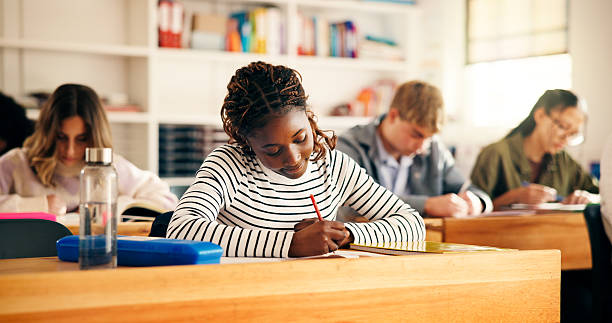istock High school students, girl and writing in lesson for assessment quiz, evaluation test or learning. Teenager, education and people with exam essay in classroom for scholarship or curriculum knowledge 2241360596