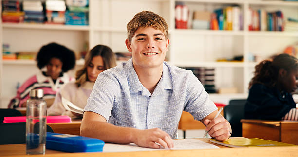 istock Portrait, high school and boy in classroom, students and writing tests with assessment. Teenagers, development and knowledge with exam, assignment and learning with education, smile and confident 2241360611