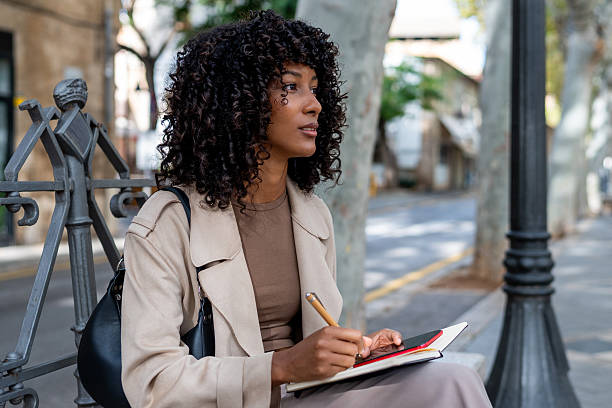 istock Young woman writing notes on city bench 2241362320