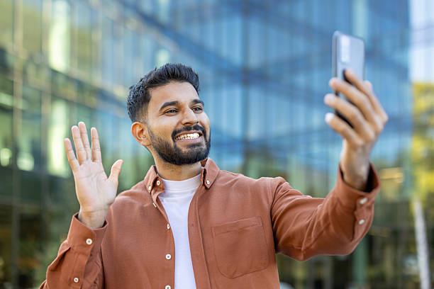 istock Happy man waves during a video call in front of a modern building 2241365205