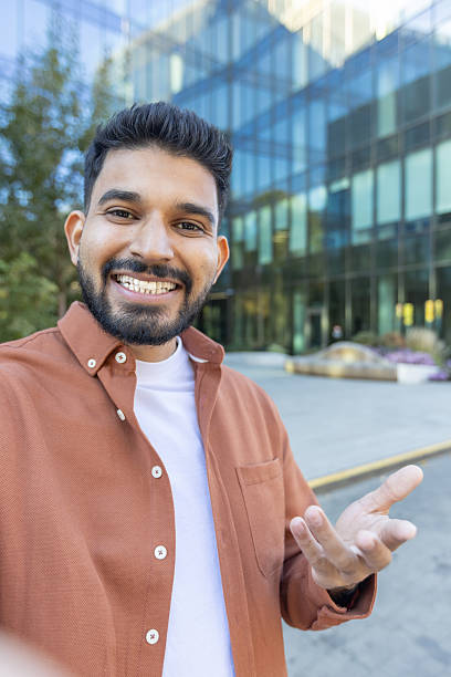 istock A man smiling and gesturing with his hand during a video call with a modern building in the background. He is friendly. 2241365217