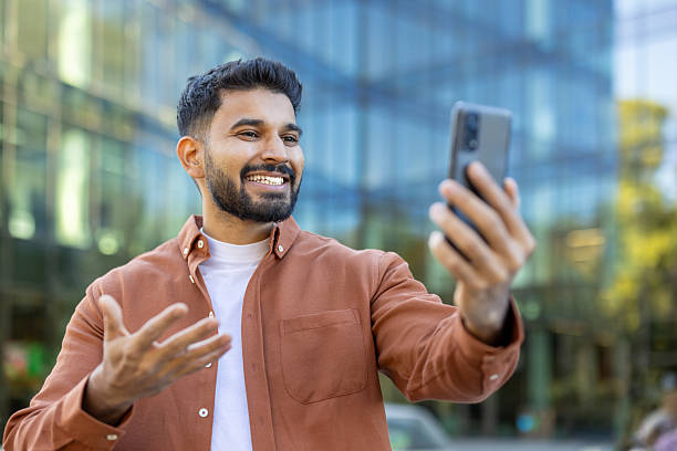 istock A smiling man holds up his phone, engaging in a video call outside a building. 2241365221