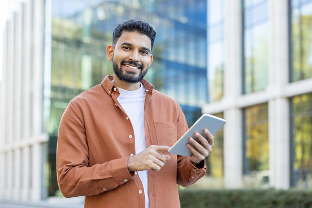 istock Smiling man outdoors using a tablet near a modern glass building 2241365247