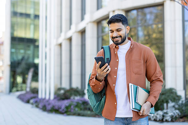 istock A student on campus looks at his phone and smiles with a backpack and books. 2241365342