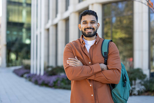 istock Smiling young man with backpack standing in front of modern building 2241365346