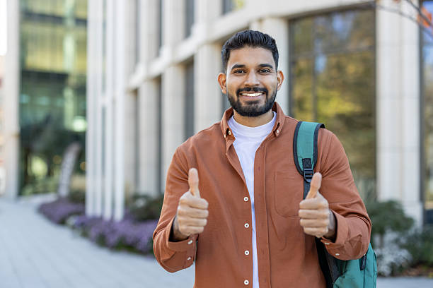 istock Smiling young man with backpack outdoors giving a confident thumbs up gesture 2241365368