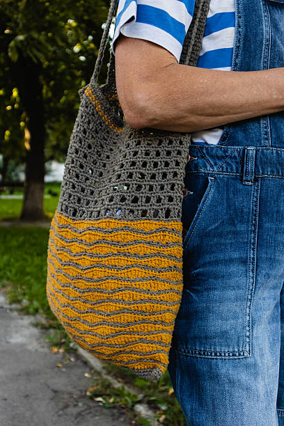 istock Yellow gray crocheted bag on a woman's shoulder during a city walk. 2241371411