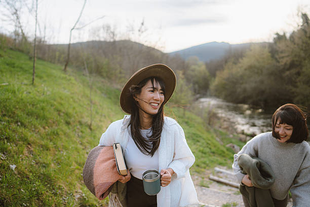 Photo of a two young women taking a day off to relax, drink coffee and read books, while making their friendship stronger on a beautiful autumn day they are spending on a remote location