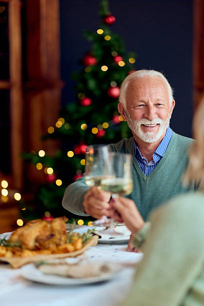istock Warm Christmas Dinner With Elderly Man Toasting Glasses In Front Of Tree 2241373024