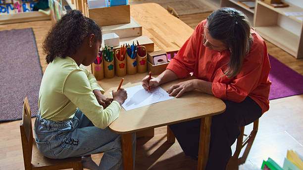 istock Teacher supporting young girl with drawing activity in classroom therapy session 2241373310