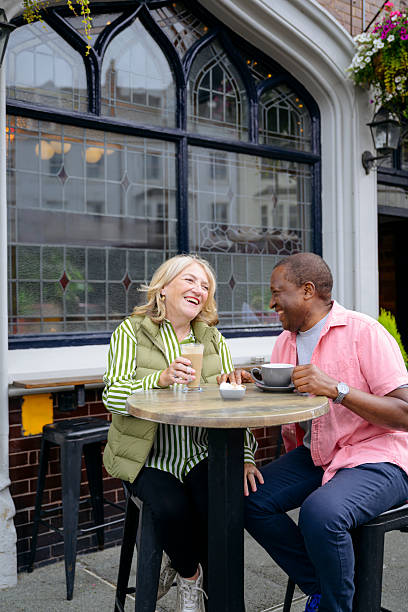 istock Cheerful senior couple sitting at table drinking coffee outside pub, smiling and laughing 2241374716