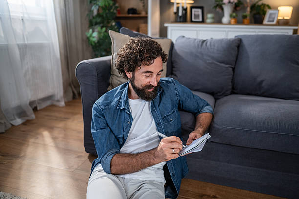 istock Man journaling in notebook sitting on living room floor 2241375889