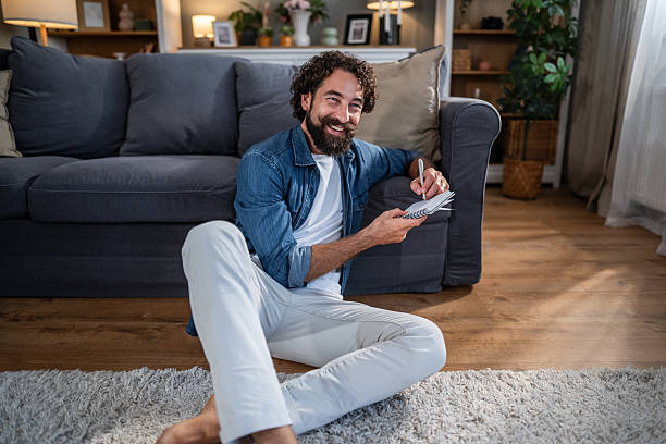 istock Happy man writing in notepad in living room 2241376449