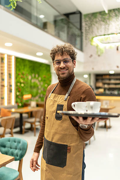 istock Waiter smiling cheerfully holding tray with two coffee cups 2241378795