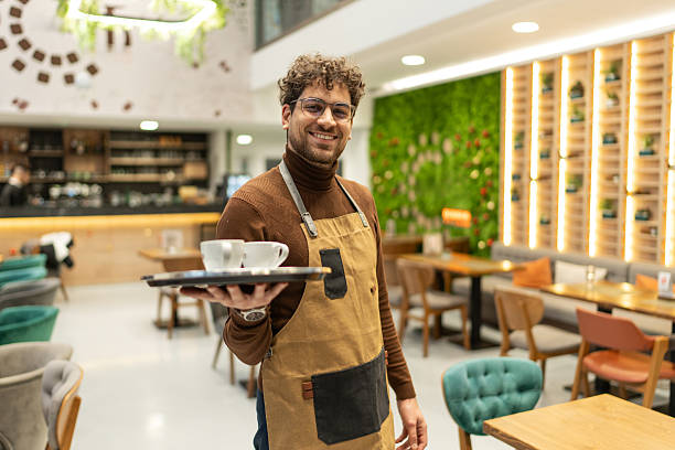 istock Waiter smiling, holding coffee cups on tray in cafe 2241378803