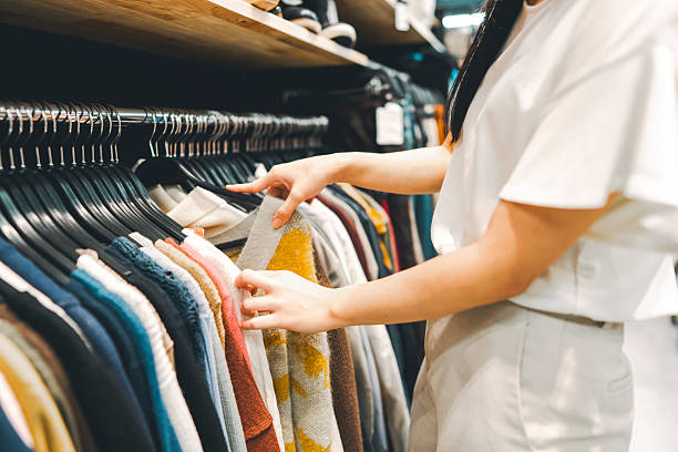Shopping cheap price at second hand clothes shop concept. Woman arm choosing trousers used clothing hangers shelf.