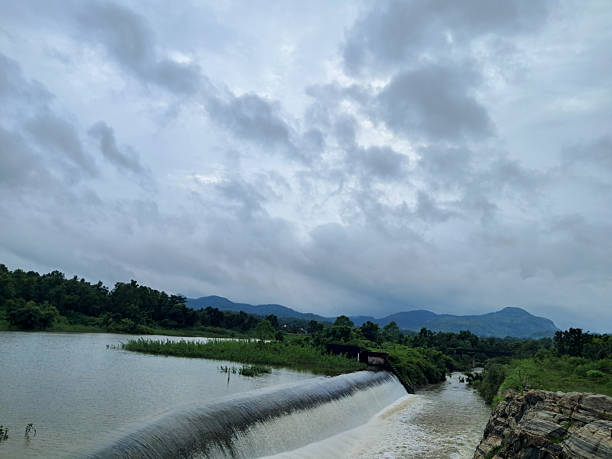 Dam Spillway and Waterfall Flowing into Reservoir Under Dramatic Cloudy Sky.