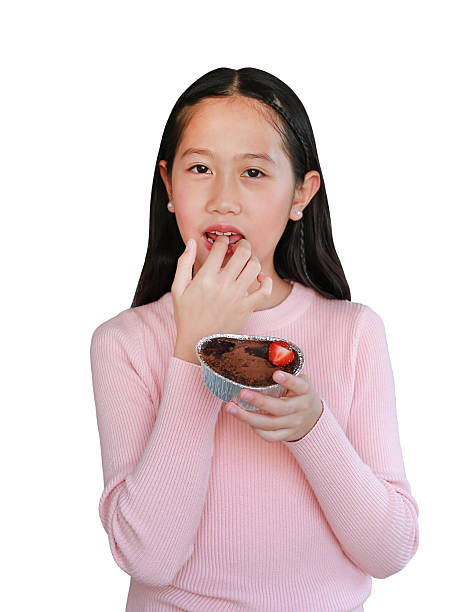 Asian girl child eating chocolate cake by index finger isolated on white background. Image with clipping path.