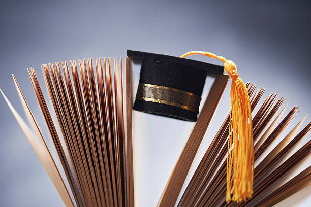 istock small mortarboard  in between of open book against chalkboard. 2241388399