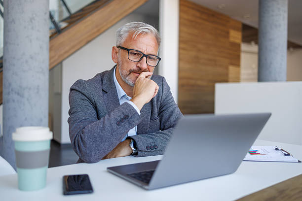 istock Confident mature businessman thinking while using laptop in office 2241391592