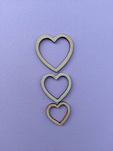 istock A minimalist composition featuring three natural wood heart shapes stacked along a lavender-purple backdrop. The simple, rustic design conveys love, connection, and tenderness, suitable for romance 2241394417