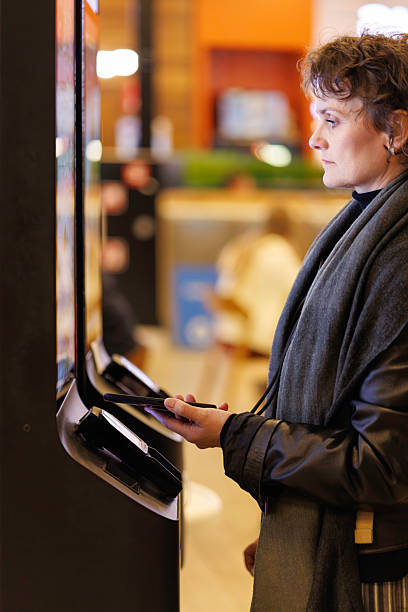 istock Woman at a self-service restaurant kiosk places an order using a handheld payment device today 2241394587