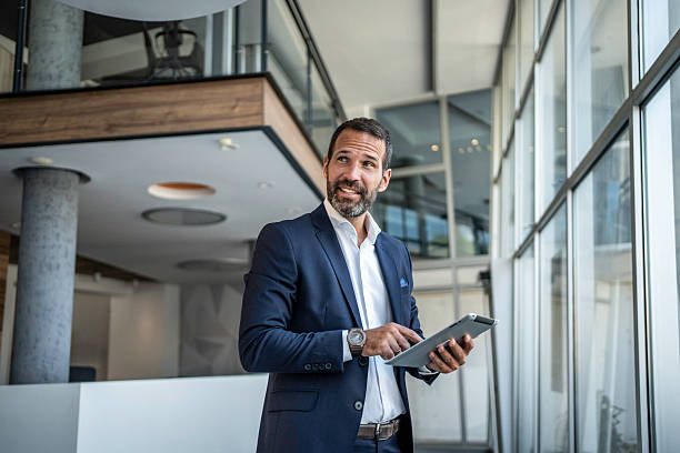 istock Confident businessman standing in modern corporate office holding tablet 2241394786