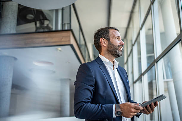 istock Businessman looking out window holding digital tablet 2241394861