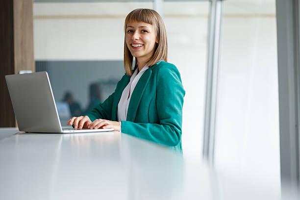istock Young businesswoman smiling, typing on laptop while working in a bright modern office environment 2241399057