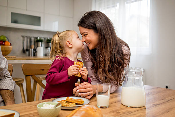 istock Single mother and her little daughter having breakfast together in a bright modern kitchen. Morning sunlight, cozy family atmosphere, and happy moments filled with warmth, care, and love. Concept of positive lifestyle and motherhood 2241401190