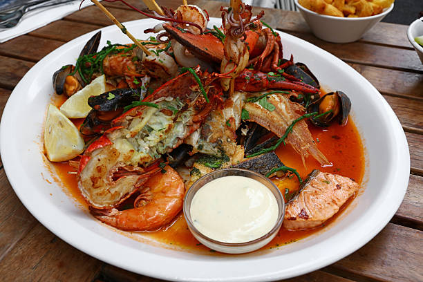 Abundant seafood platter presenting a variety of fresh ingredients including lobster, prawns, mussels, and fish in a rich sauce, served with lemon wedges and a dipping sauce