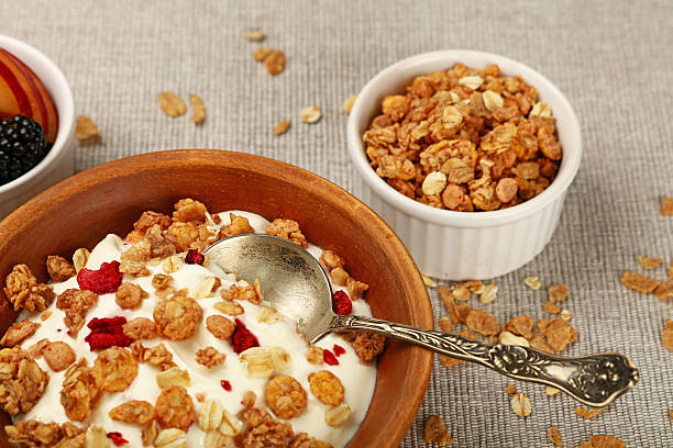 Healthy breakfast bowl of creamy yogurt with crunchy granola, dried raspberries, and an ornate silver spoon, alongside fresh sliced peach and blackberries